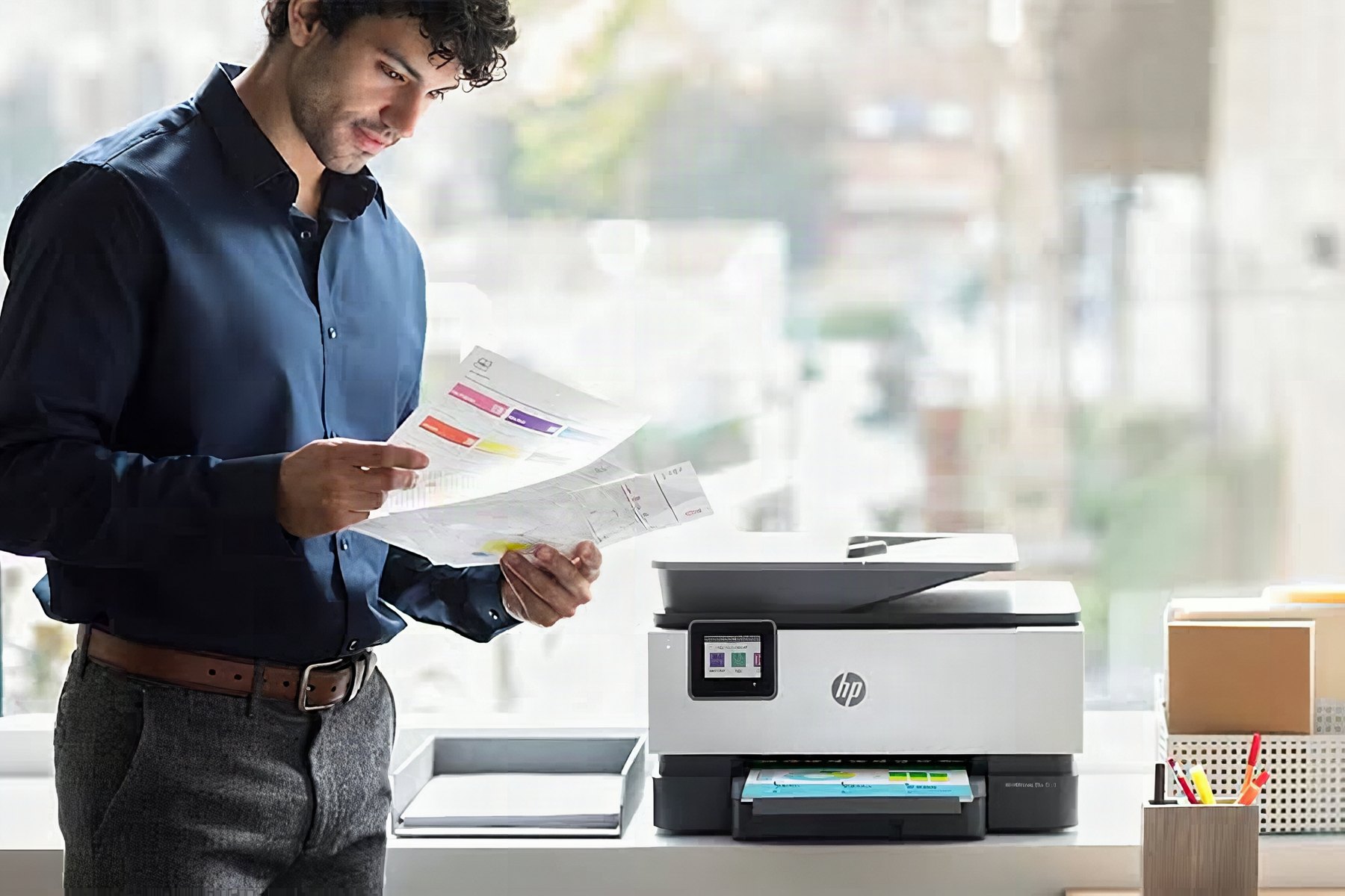 Profesional revisando impresiones junto a un multifuncional HP OfficeJet Pro, distribuido por Teamreca en Caracas